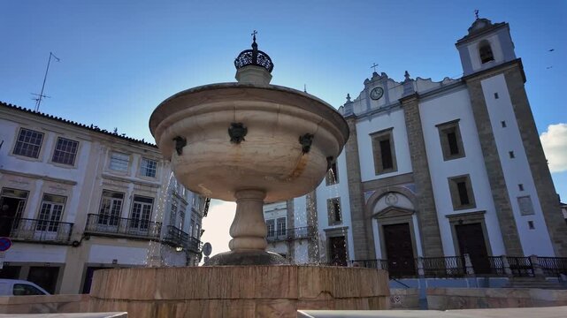 Stone fountain in front of baroque church at sunny day in historic European town square.