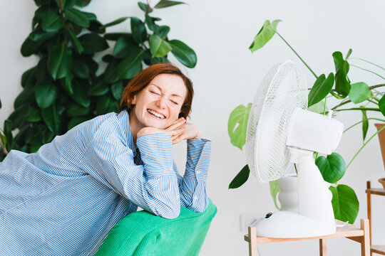 A laughing woman cools herself by an electric fan at home