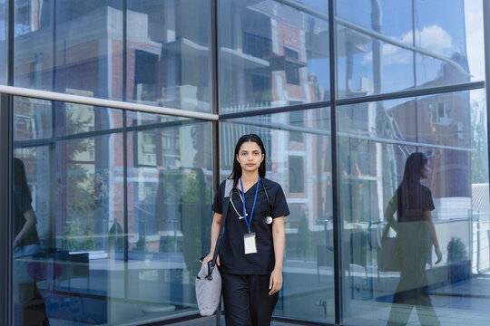 Female doctor takes a pause outside a modern glass hospital
