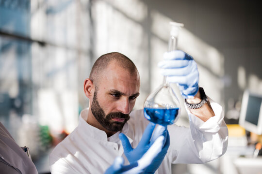 Male scientist analyzes blue liquid in a laboratory flask