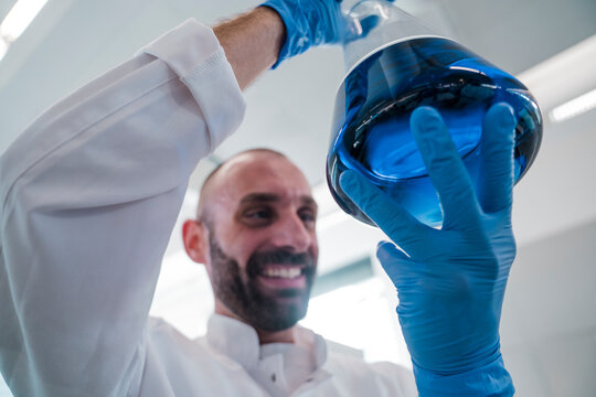 Smiling male scientist holds a flask with blue liquid in laboratory