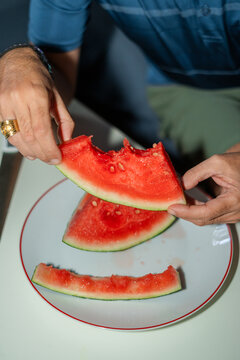 Man holds a bitten slice of fresh watermelon over a plate