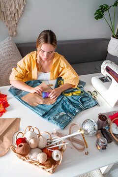 Female designer upcycles denim clothing at a table indoors