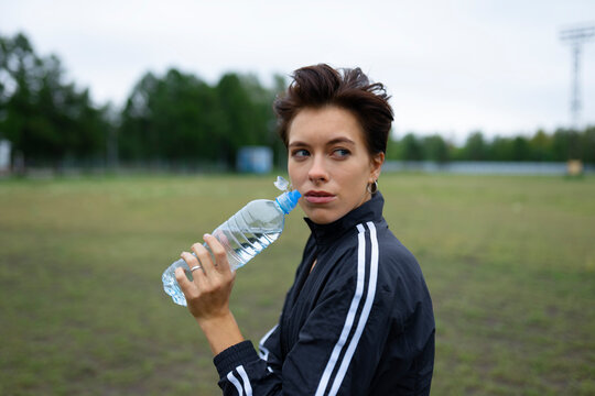 Athletic young woman holds a water bottle on a sports field