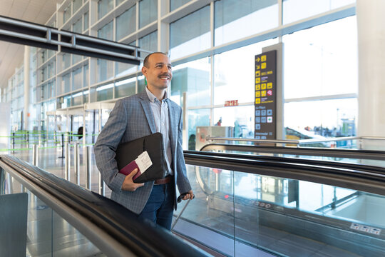 Smiling businessman with luggage on moving walkway at the airport