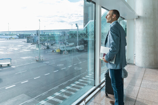 Businessman waits with luggage at the airport window in Barcelona