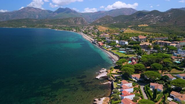 Saint-Florent Corsica drone backward reveal Citadel marina bay turquoise sea. Aerial overflight of historic round fortress, old town pastel houses, yacht harbor, surrounding mountains 4K video.