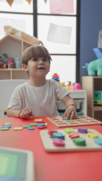 Boy placing a wooden puzzle piece with hand at a red play table in a building playroom surrounded by colorful toys and shelves; concentration.