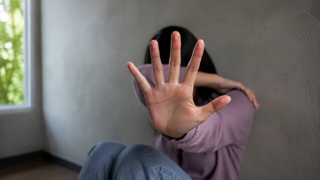 Woman's hand raised stopping abuse in domestic violence situation with soft window light and selective focus
