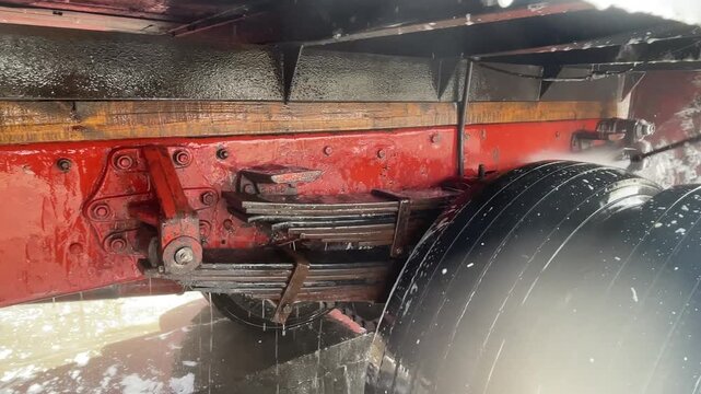 Rear wheel and lower side of a red truck are cleaned with water and foam, showing tire washing, underbody care and removal of accumulated road dirt during a carwash. during routine cleaning.
