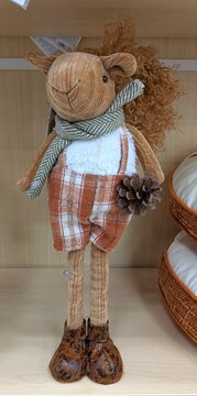 Tiempo de oto&ntilde;o. Simp&aacute;tico mu&ntilde;eco de ardilla de estilo artesanal, con bufanda, pantal&oacute;n corto y sujetando una pi&ntilde;a de pino, de pie en el estante de un comercio	