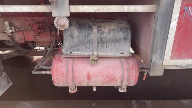 Close-up of the lower rear section of a heavy truck at a carwash, showing a large cylindrical tank, brackets, frame parts, and dirty metal surfaces during washing and cleaning work for stock use