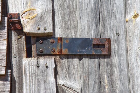 Rusted iron door latch hasp on weathered wooden barn door texture background