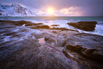 Fototapeta premium Scene featuring beach of Norwegian sea on rocky coast in fjord on sunset in winter. Vareid beach, Lofoten islands, Norway