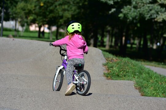 Young girl wearing a safety helmet riding a bicycle on a pump track in a sunny green park, practicing cycling skills and enjoying active outdoor recreation, exercise and childhood adventure.