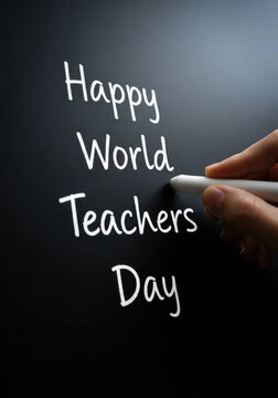 Hand writing happy world teachers day on a black chalkboard with white chalk