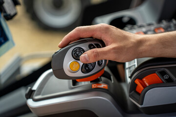 Operator hand holding modern multifunctional control joystick with buttons and emergency stop switch inside agricultural tractor vehicle cabin. © Marina