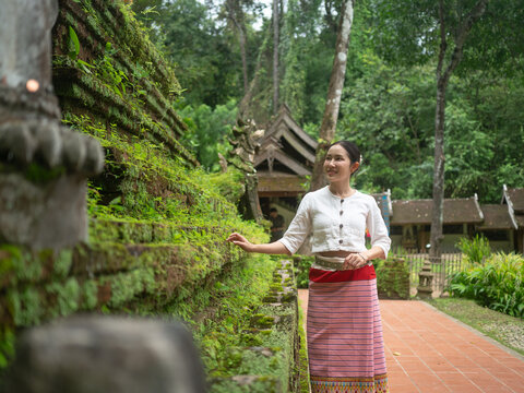 Asian woman in traditional Thai dress standing near mossy ancient pagoda in temple garden, Jae Dee Wad Palad