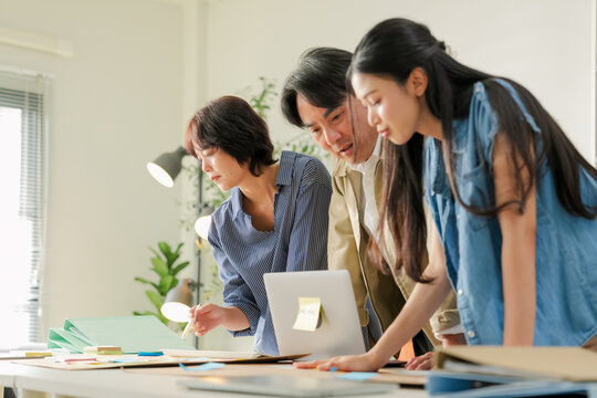 Team leaning over desk discussing strategy chart together, one colleague laughing while others focus intently, casual collaborative brainstorming session concept