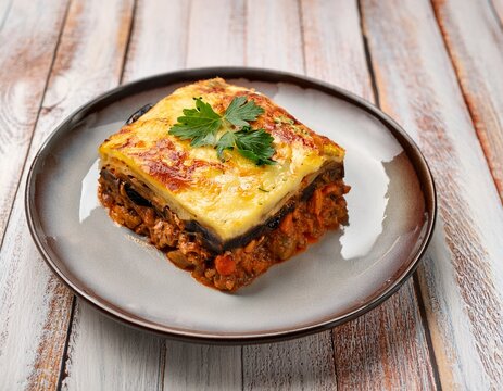 a delicious portion of traditional greek moussaka with eggplant and meat sauce on a rustic white wood surface