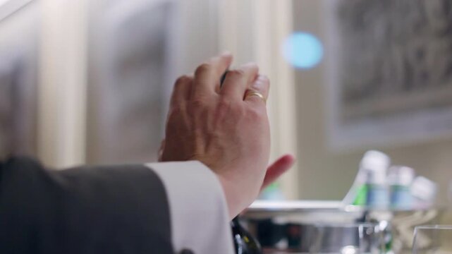 Waiter in uniform using corkscrew for uncorking bottle of wine or champagne, spiral corkscrew pulling stopper from the neck of the bottle, catering service in luxury restaurant
