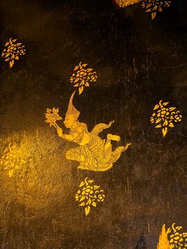 Close up of traditional Thai golden mural painting of a Deva angel on a dark textured background at Wat Phra Phuttha Chinnarat, Thailand.