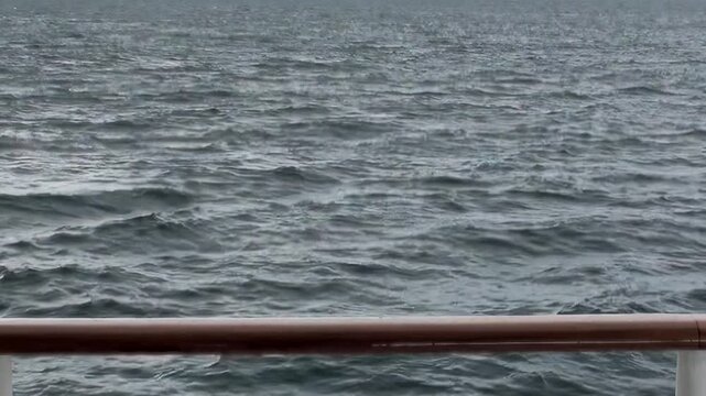 The Arctic Ocean is viewed from a ship deck and railing, with cold open water extending toward the distant polar horizon during a northern sea voyage. The source identifies the location near Norway.