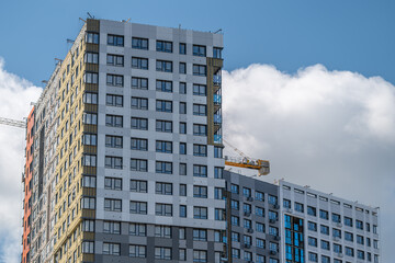 Modern building under construction against a bright blue sky featuring clouds and cranes in a bustling city environment © beholdereye