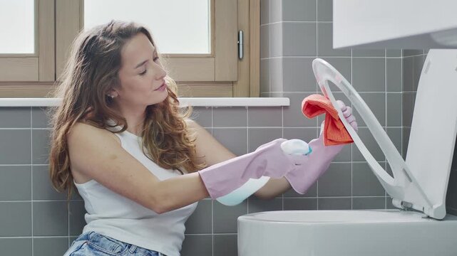 Woman Cleaning and Sanitizing Toilet Seat with Spray Detergent in Bathroom