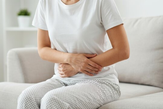 Woman sitting on a sofa holding her stomach due to abdominal pain or discomfort