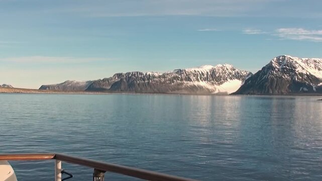 Snow-covered Arctic mountains rise beyond the cold ocean, forming a remote northern seascape with broad water, rugged peaks, and polar atmosphere. The source identifies the location near Norway.