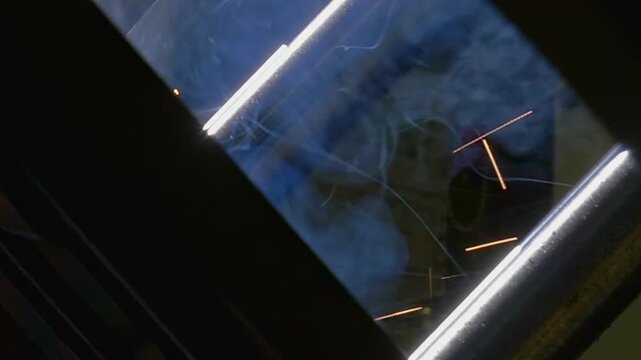 A robotic argon welding arm joins metal pipe sections with controlled motion during an industrial welding process. Bright sparks flare around the welding area as the process continues.