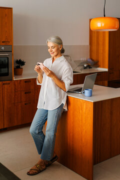 Woman browsing smartphone while relaxing in kitchen