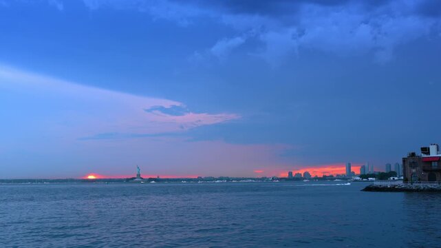 View on New York Harbor at dusk time. The Statue of Liberty and red light in the sky in the backdrop.