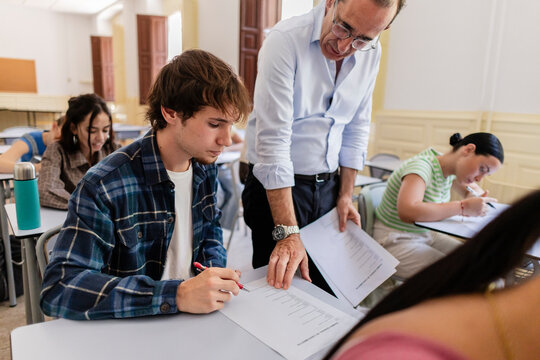 Teacher helping young male student with written exam