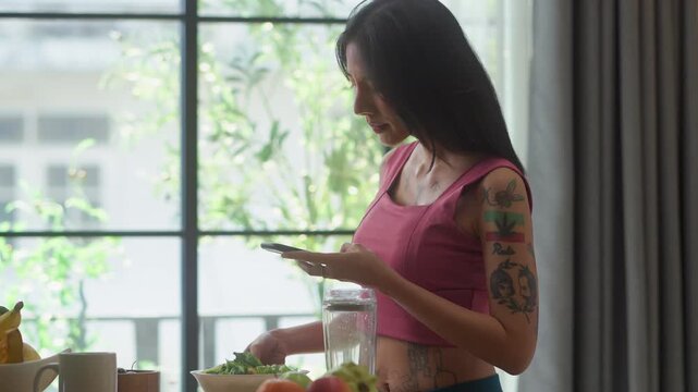Woman photographing smoothie ingredients with smartphone in kitchen, capturing healthy recipe content for social media, satisfied smile during meal prep documentation concept