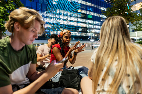 Diverse friends talking and using mobile phones at night