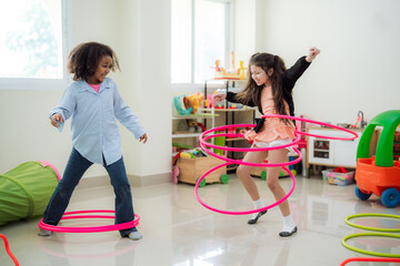 Happy diverse kids laughing and exercising with hula hoops in a kindergarten playroom, highlighting multicultural friendship, active child development, and fun physical activities. © VStudio