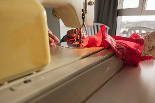 Senior woman sewing red fabric with machine at home