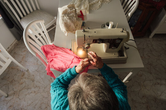 Senior woman sewing clothing with machine at home