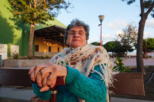 Senior woman relaxing on park bench holding walking stick