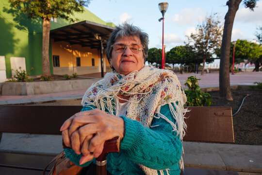 Senior woman relaxing on park bench with walking stick