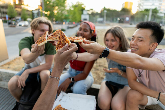 Diverse friends sharing pizza slices outdoors, enjoying connection