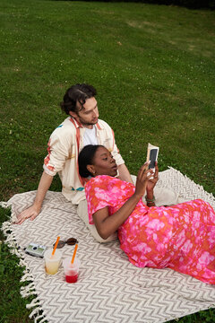 Couple on a blanket looks at a phone in a park