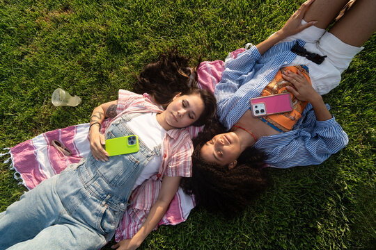 Friends Relax  Holding Phones in Park