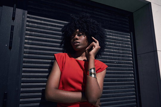 Woman in red dress poses against black wall