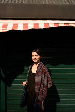 Woman Stands Under Striped Awning at Green Shop Entrance