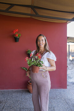 Smiling pregnant woman holding a potted plant on porch at home