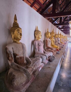 Perspective view of ancient seated Buddha statues lined up in a temple cloister gallery in Thailand.
