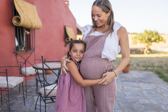 Little girl hugging her pregnant mother's belly in the garden at home